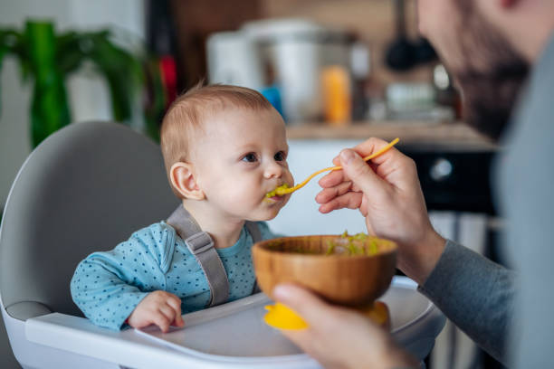 Caring single father spoon feeding his beautiful son at home.